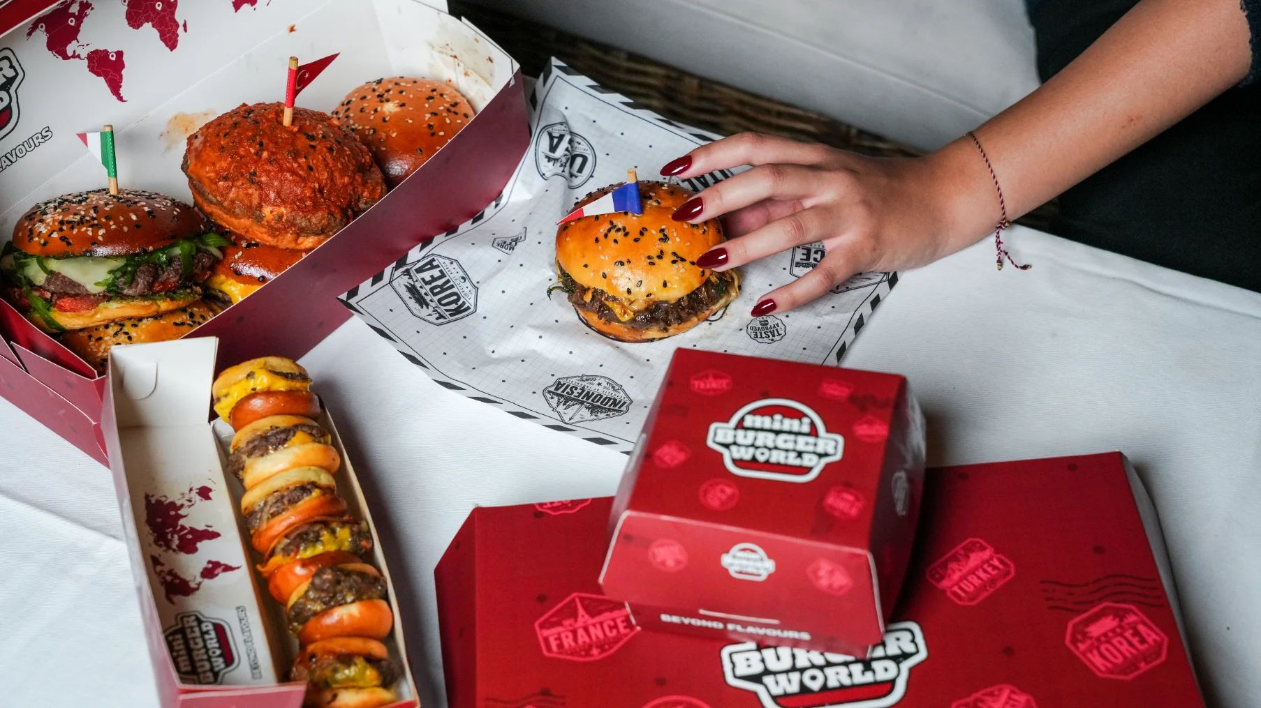 A table of Mini Burger World burgers: a box of flagged burgers, a row of mini burgers and a hand reaching for one